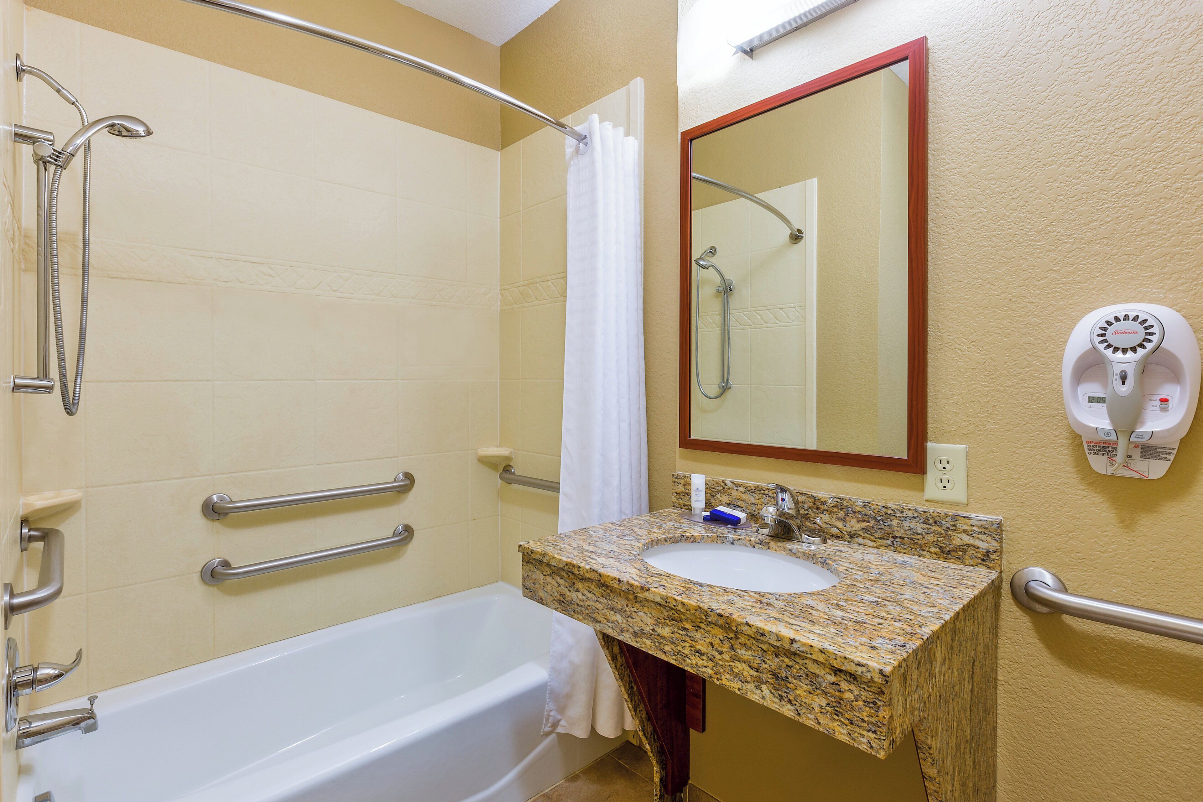 A bathroom with a bathtub, a sink, a mirror, a shower, and a hand dryer.