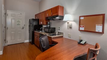 Una cocina compacta con armarios de madera, un refrigerador, un microondas y una estufa. Hay una mesa de comedor con sillas, una lámpara y un teléfono sobre la mesa.