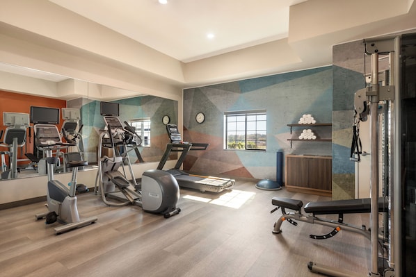 A gym with cardio machines, a bench press, and a mirrored wall.