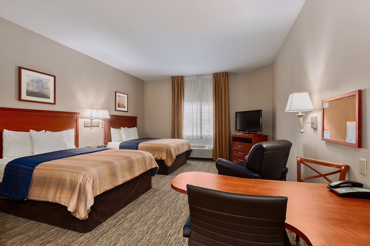 A hotel room with two beds, a desk, a chair, a TV, and a window with curtains.