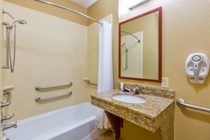 A bathroom with a white bathtub, a granite sink, a mirror, and a hand dryer.