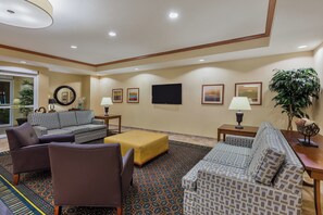 A hotel lobby with a sofa, armchairs, a coffee table, a TV, and a plant.