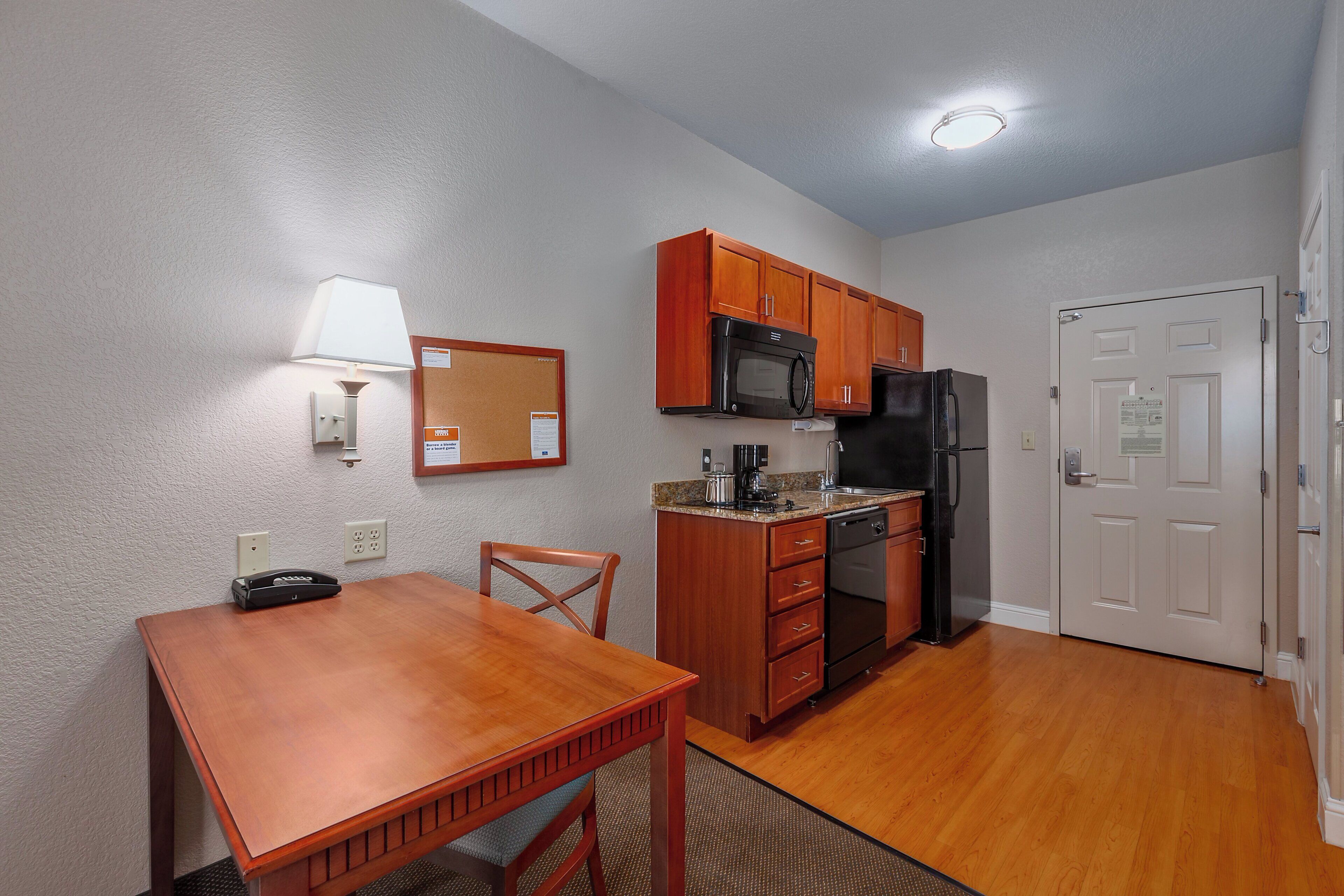 A compact kitchen with wooden cabinets, a microwave, a refrigerator, and a dining table with chairs.