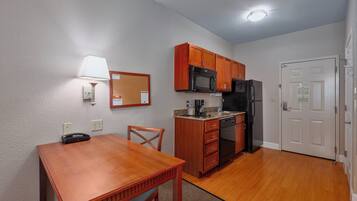 A compact kitchen with wooden cabinets, a microwave, a refrigerator, and a dining table with chairs.