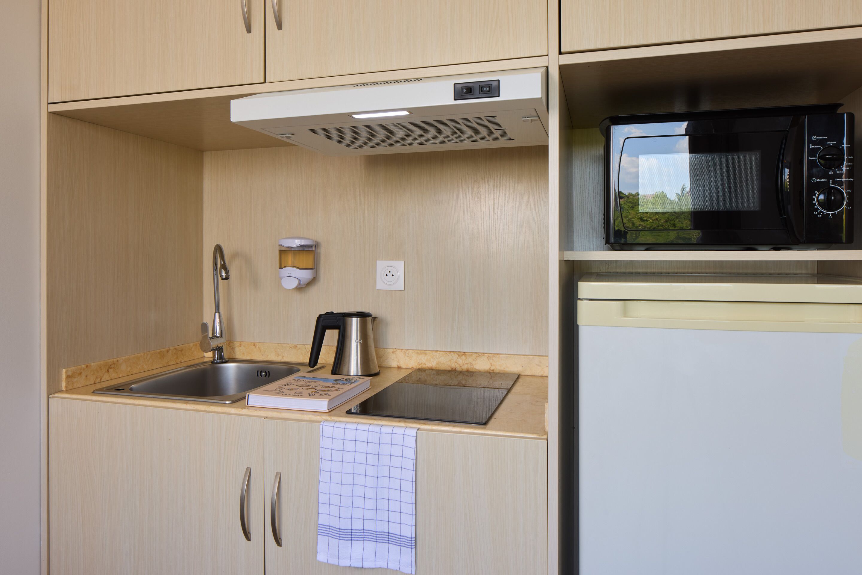 Een kleine keuken met een spoelbak, waterkoker, magnetron en een koelkast.