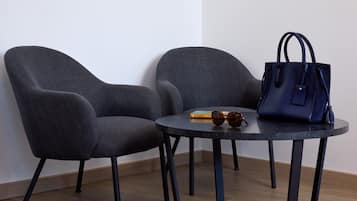 Dos sillones grises, una mesita redonda con un tapete tejido y un bolso azul oscuro.