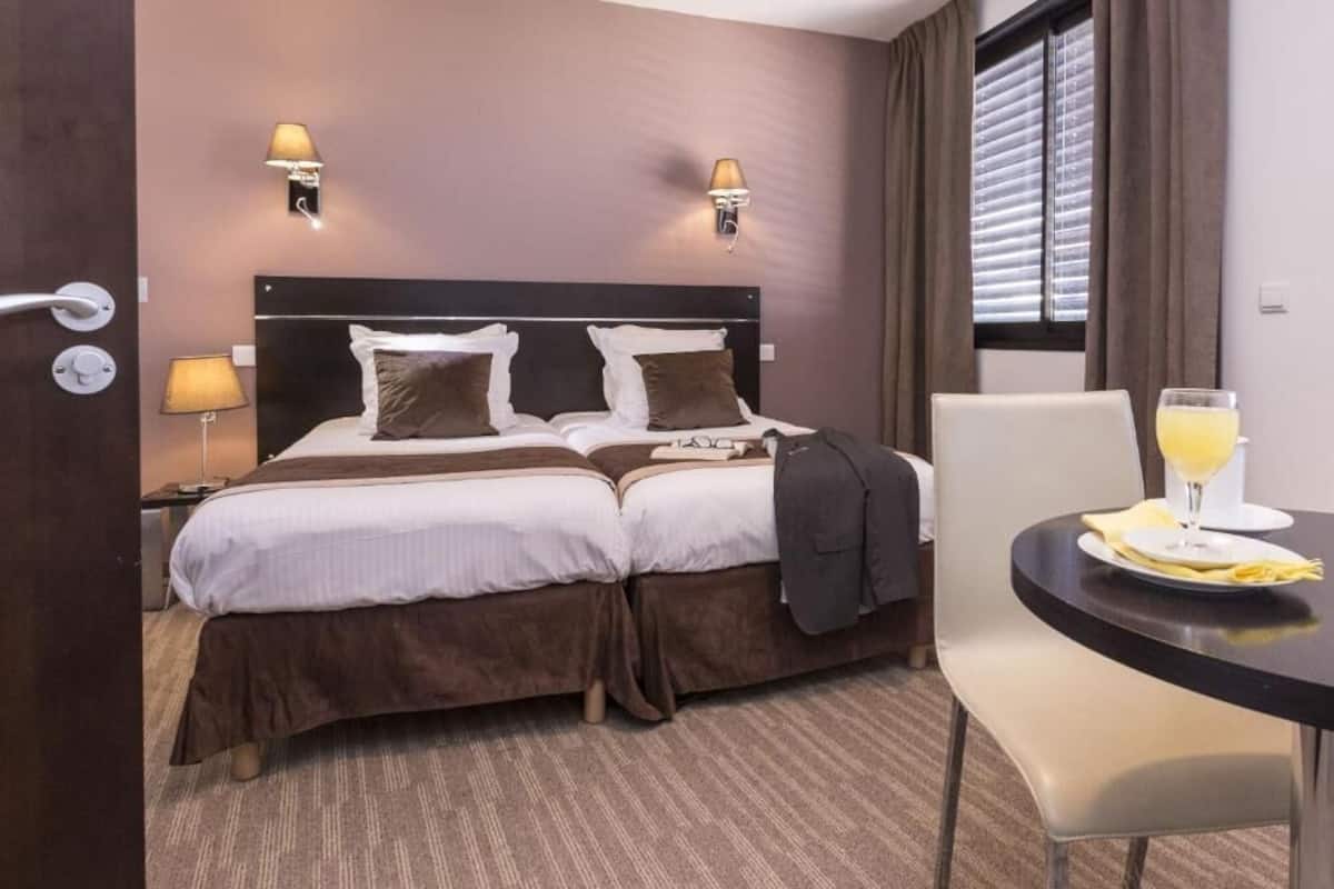 Een hotelkamer met een tweepersoonsbed, twee bedlampen, een tafeltje met een glas sinaasappelsap en een stoel.