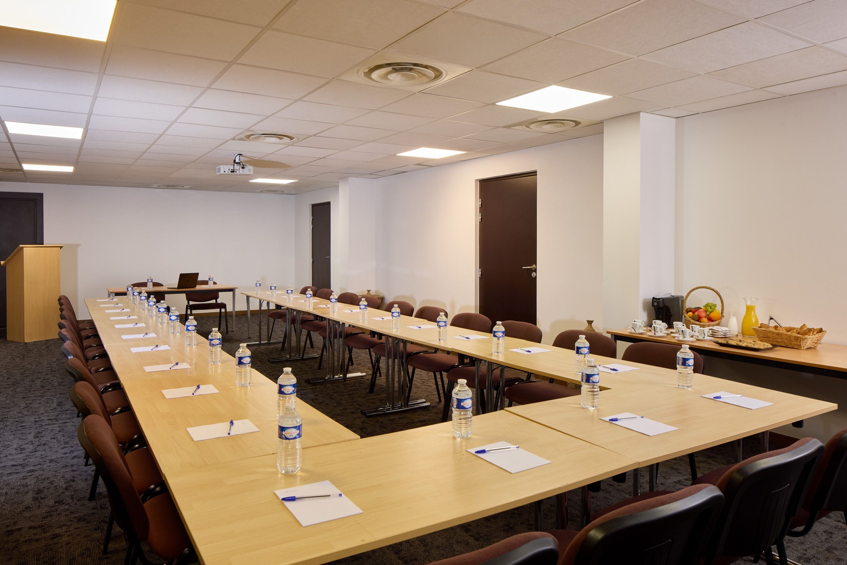 A conference room with long tables, chairs, water bottles, and a podium.