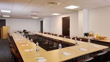 Un salón de conferencias con mesas largas, sillas, botellas de agua y un atril.