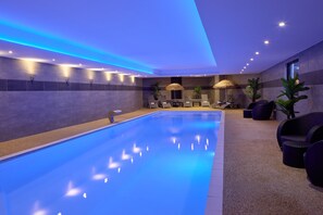 A swimming pool with a blue tint, surrounded by lounge chairs and a seating area with umbrellas.