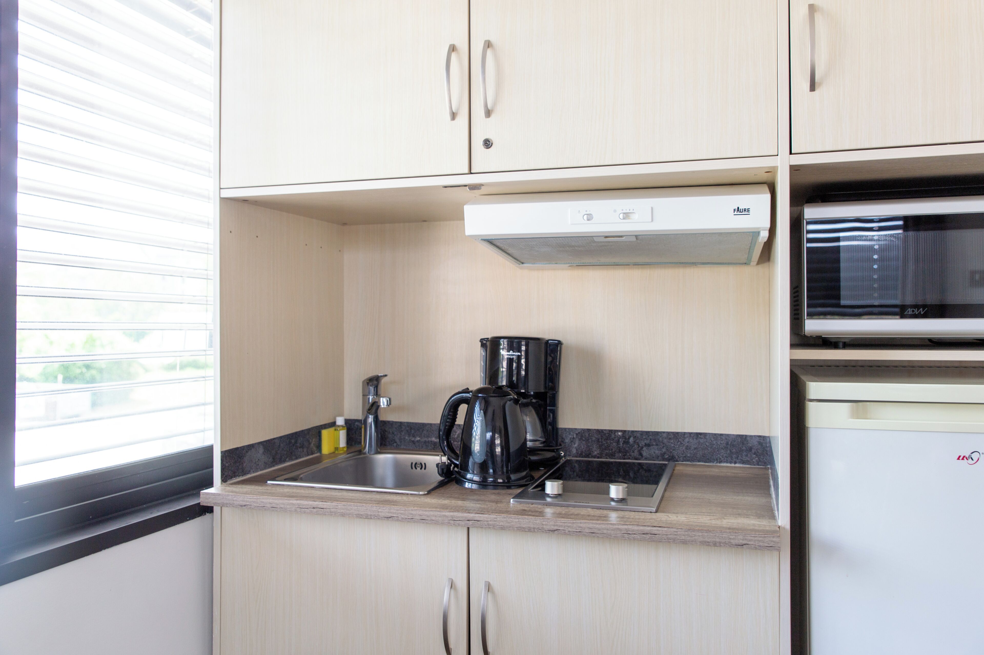 A compact kitchen with a built-in microwave, a coffee maker, and a sink.