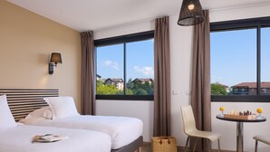Une chambre d’hôtel avec deux lits, une table à manger avec un jeu d’échecs, une chaise et une vue sur les immeubles.
