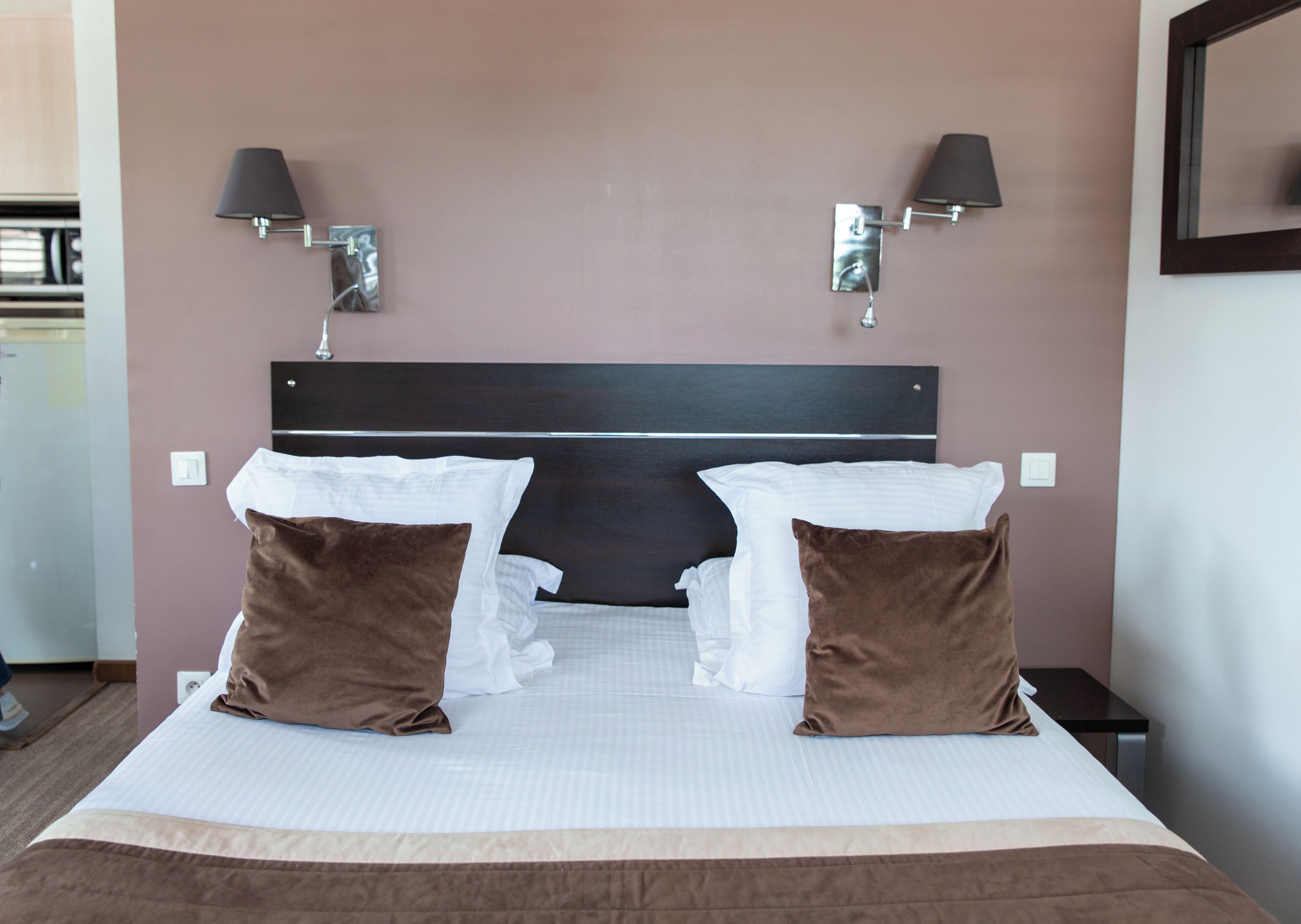 A neatly made bed with white and brown pillows, a dark headboard, and two wall-mounted lamps.