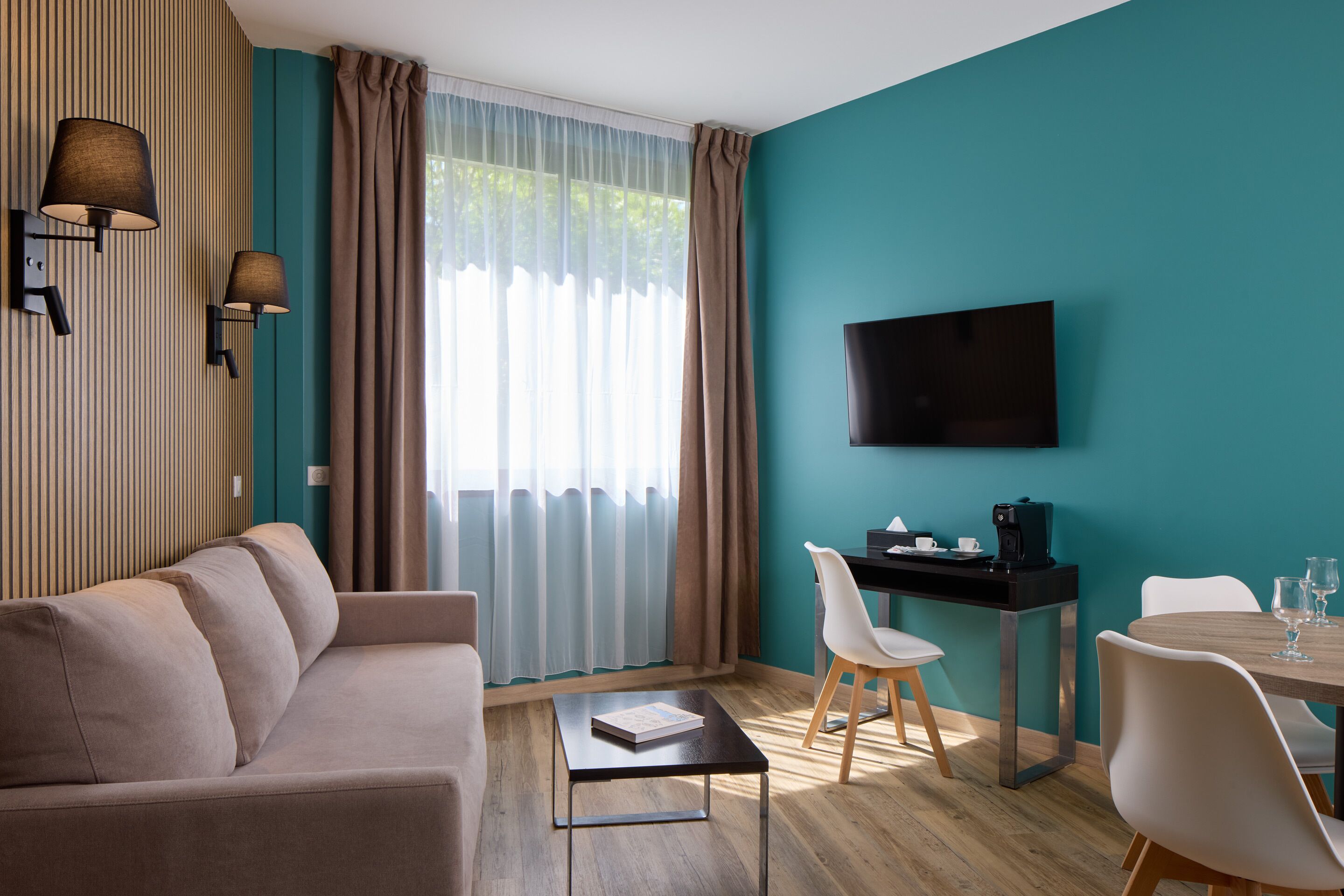 A modern room with a sofa, a small table, a desk with a chair, a TV, and a window with curtains.