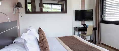 A hotel room with a bed, a desk with a chair, a television, and a window with blinds.