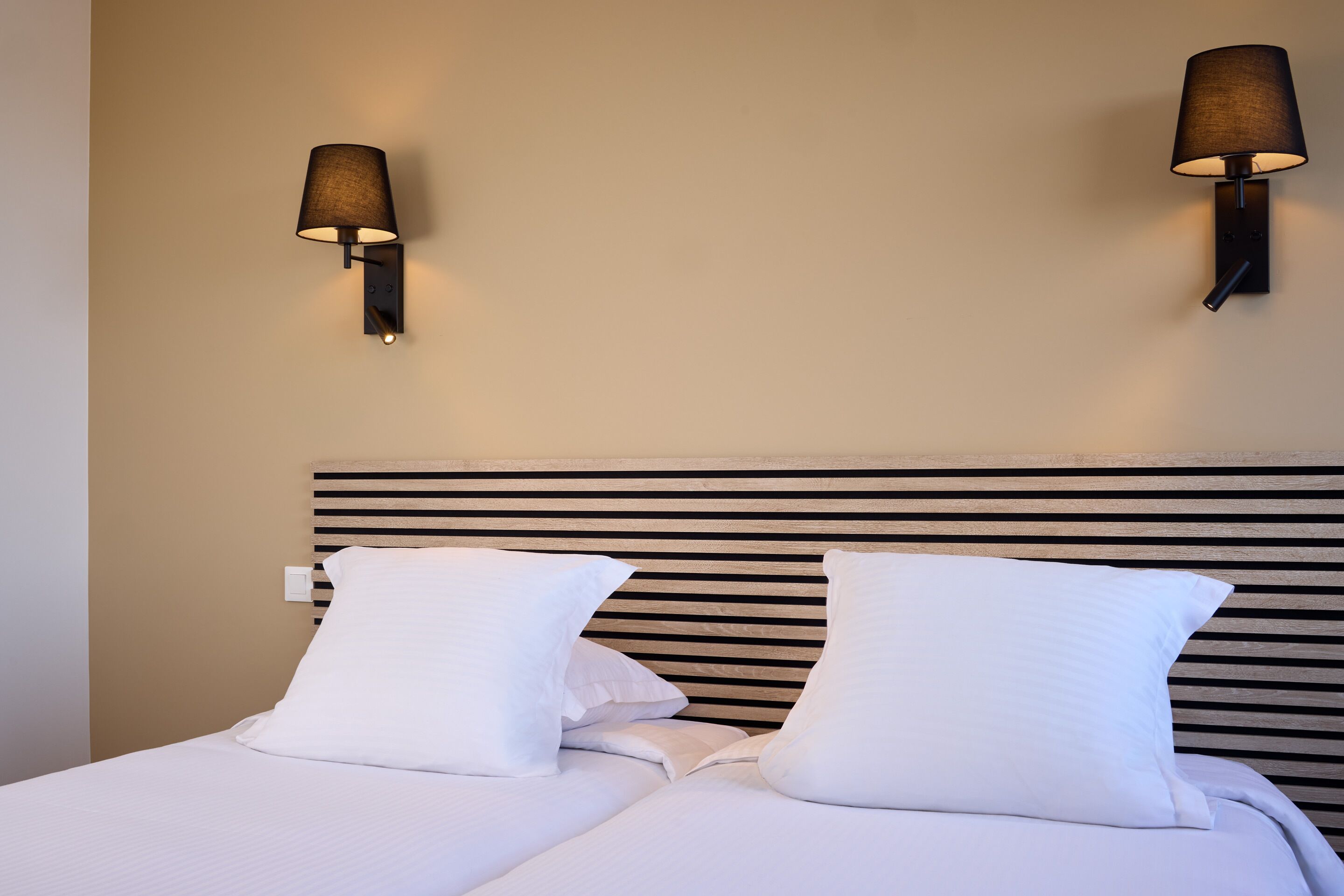 A bed with white bedding, two wall-mounted lamps, and a wooden headboard.