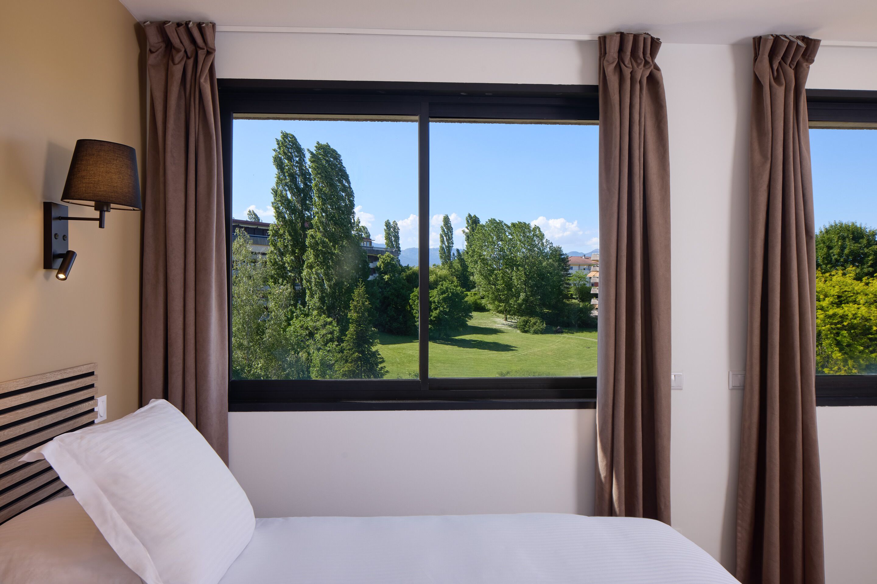 Una habitación de hotel con un ventanal grande, una cama y una lámpara de pared.