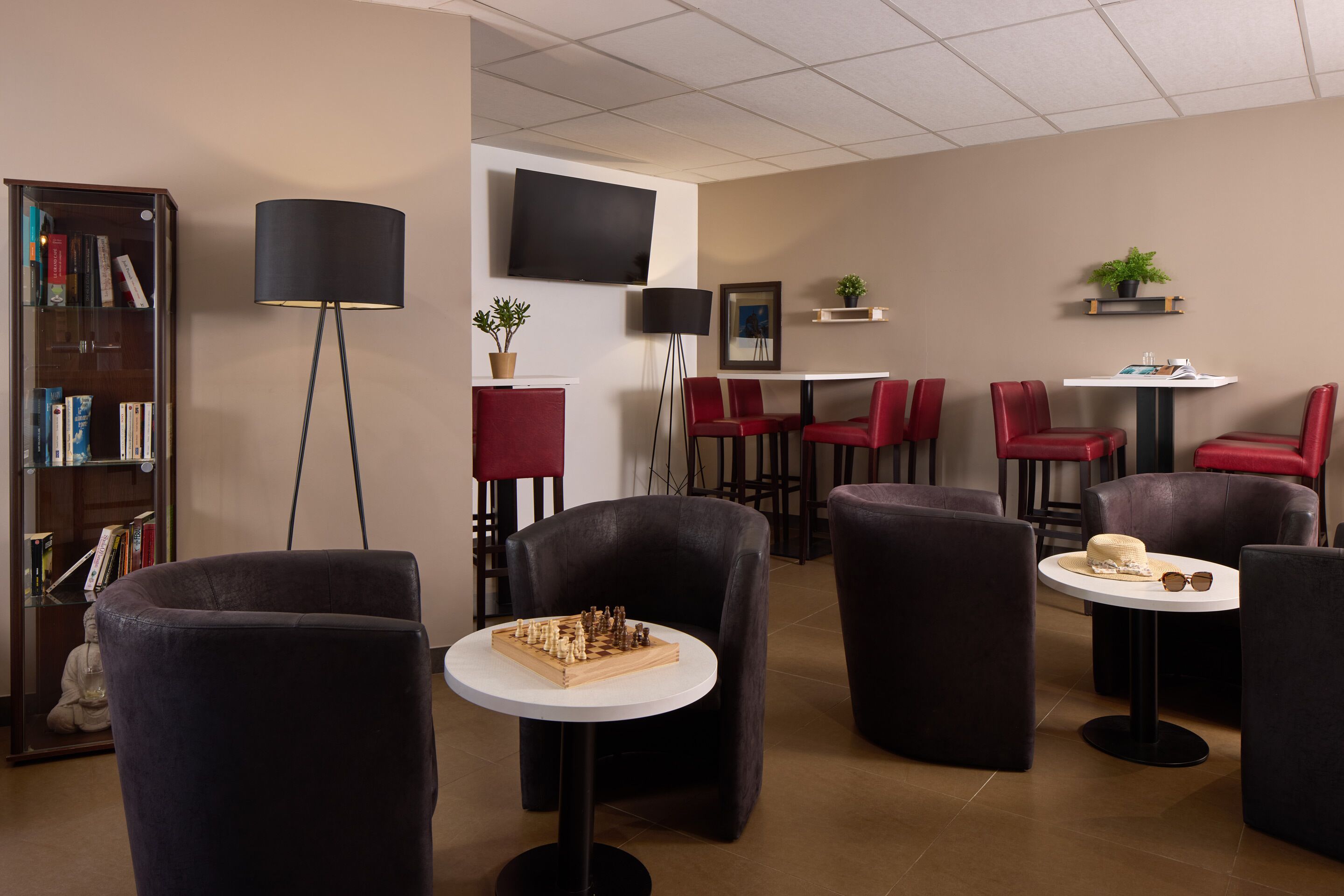 A modern lounge area with a flat-screen TV, bookshelves, red chairs, and a chessboard.