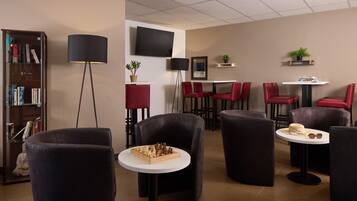 A modern lounge area with a flat-screen TV, bookshelves, red chairs, and a chessboard.