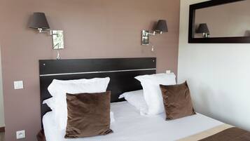 A neatly made bed with white and brown pillows, two wall-mounted lamps, and a mirror on the wall.