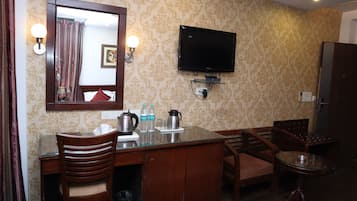 A hotel room with a wooden desk, chairs, a television mounted on the wall, and a mirror.
