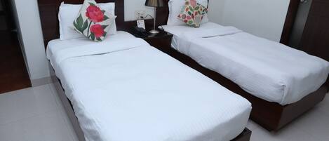 A hotel room with two single beds, a nightstand with a lamp, and a wall socket.