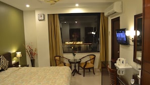 A hotel room with a bed, a desk with a chair, a television, and a window with curtains. - Hotel Hari Heritage (Haridwar)
