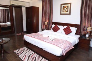 A neatly arranged hotel room with a large bed, a bedside table, a lamp, and a painting on the wall. - Hotel Hari Heritage (Haridwar)