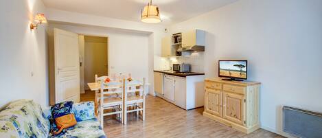A compact living space with a sofa, dining table, chairs, a kitchenette, and a television.