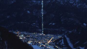 Une chaîne de montagnes enneigées, avec une ville située à son pied, et une structure lumineuse verticale particulièrement visible.