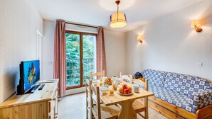 Una habitación acogedora con una mesa de comedor de madera, sillas, un sofá, un televisor y un amplio ventanal con cortinas.