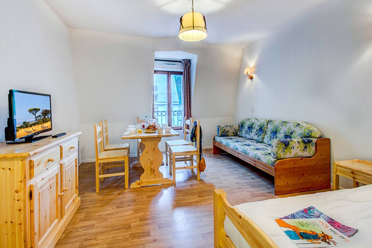 Une pièce chaleureuse avec un plancher en bois, une table à manger avec des chaises, un canapé, un téléviseur et une fenêtre avec des rideaux.