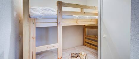 Una cama individual con estructura de madera, ropa de cama blanca y una mesita con un libro y un peluche.