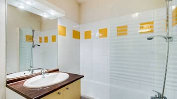 A modern bathroom with a glass-enclosed shower, a white sink with a wooden countertop, and yellow-tiled walls.