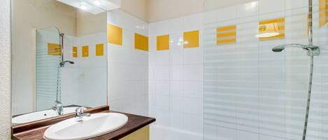 A modern bathroom with a glass-enclosed shower, a white sink with a wooden countertop, and yellow-tiled walls.
