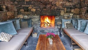 A stone fireplace with a fire, surrounded by a stone wall. There are two sofas with cushions and a wooden coffee table with a vase of flowers in the center. - Bedford Post Inn (Bedford)