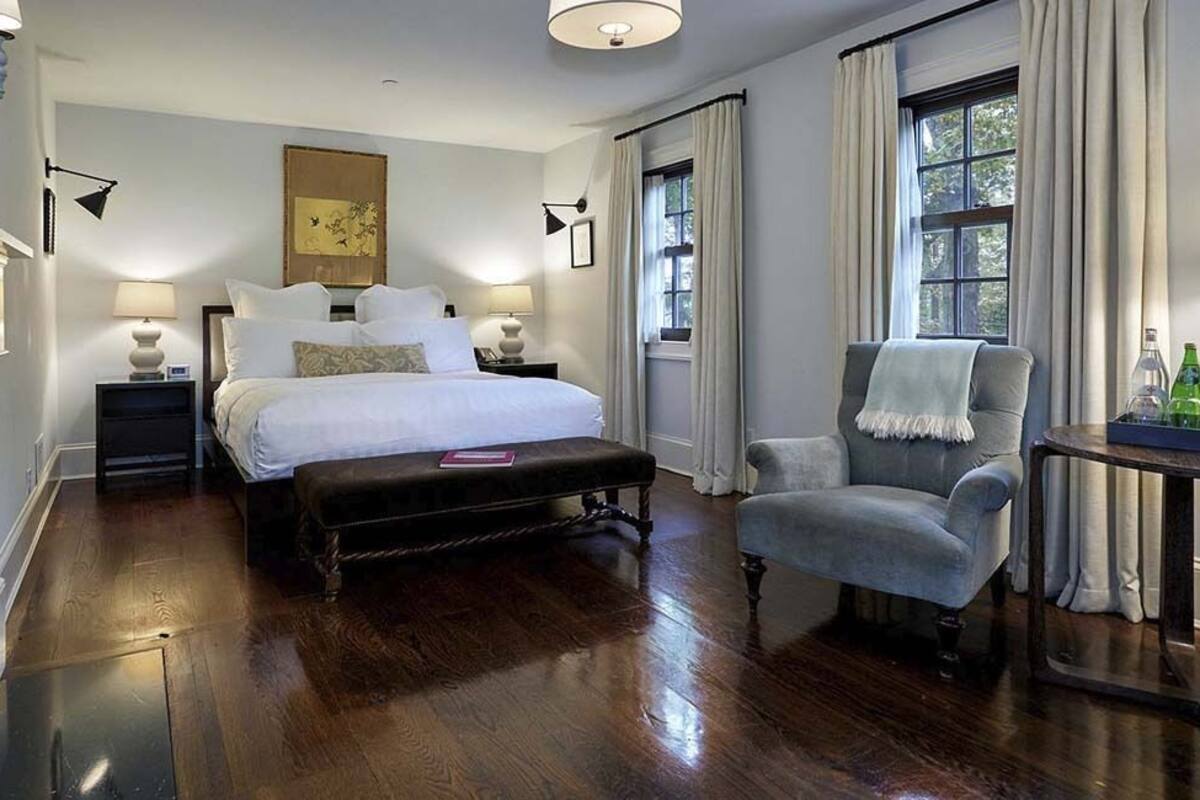 A bedroom with a large bed, a chair, a nightstand, a lamp, and a fireplace.