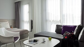 A modern hotel room with a bed, a sofa, a coffee table, and a chair. - Novotel Suites Malaga Centro (Málaga)