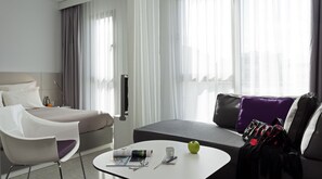 A modern hotel room with a bed, a sofa, a coffee table, and a chair. - Novotel Suites Malaga Centro (Málaga)