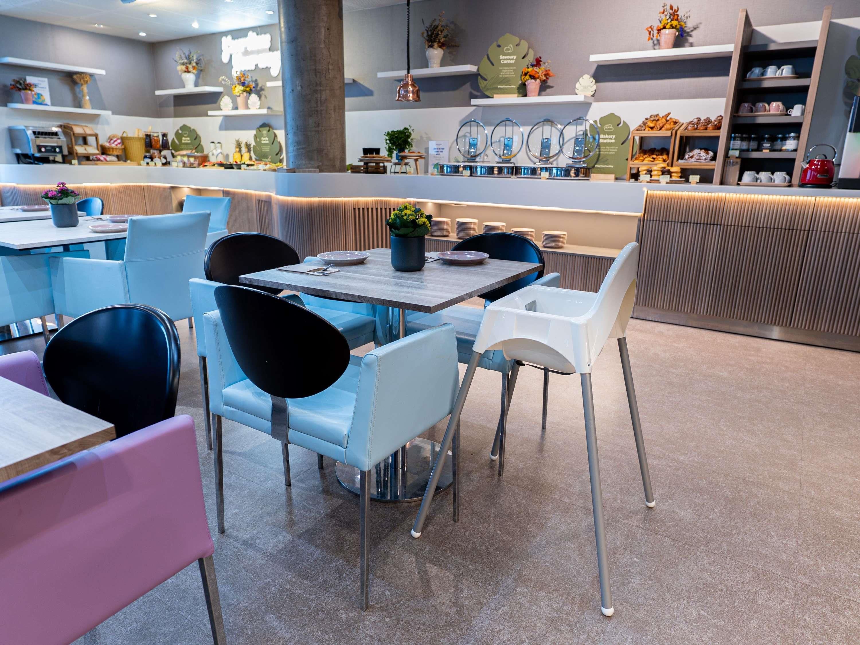 A modern cafe with tables and chairs, a counter with baked goods, and shelves with decorative items.