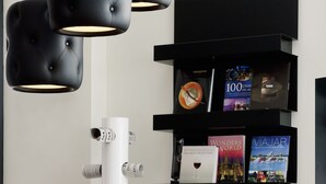 A modern hotel lobby with black tufted chairs, a white column, and a bookshelf with travel books and magazines. - Novotel Suites Malaga Centro (Málaga)