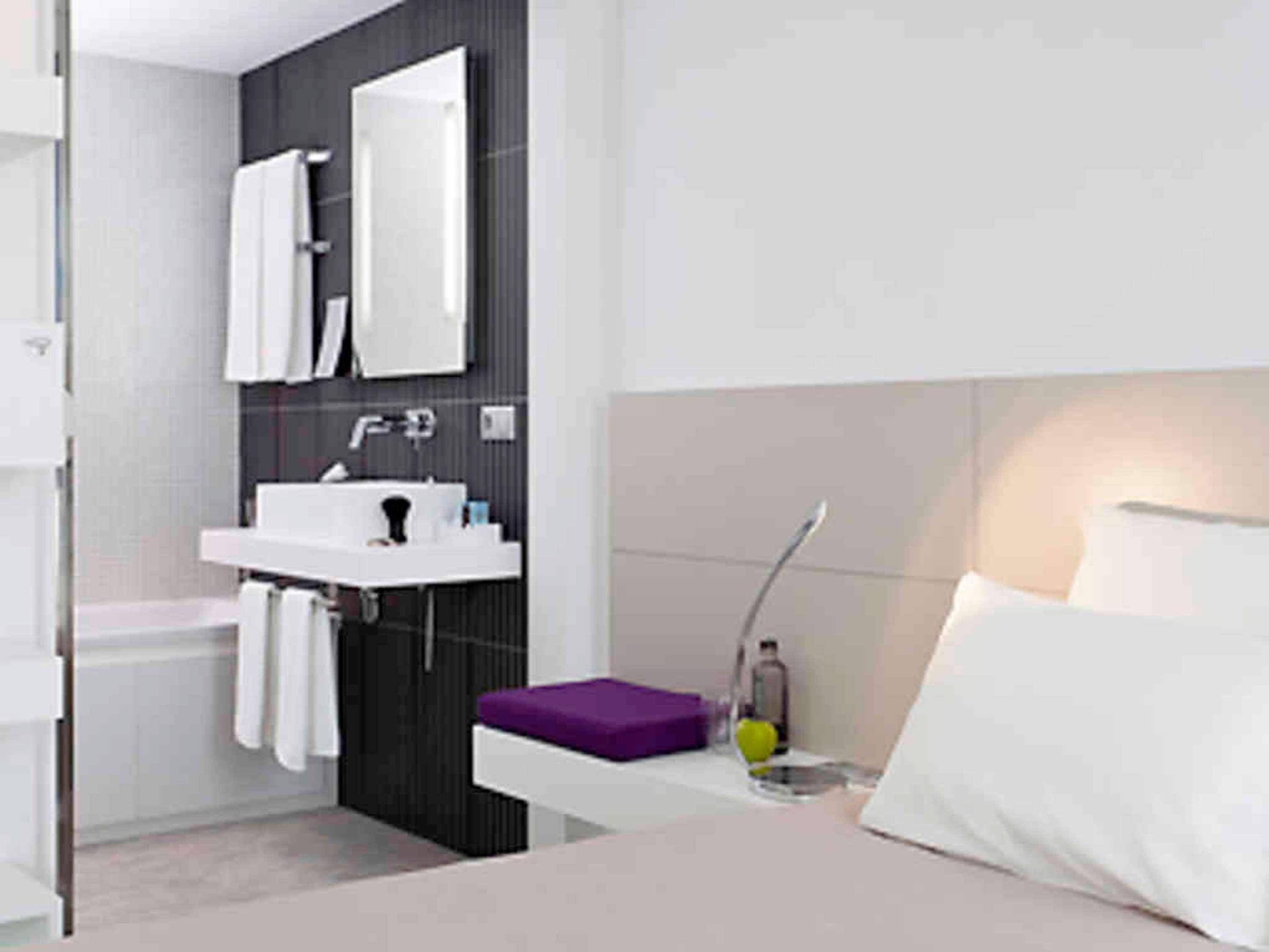 Un baño moderno con un lavamanos blanco, un espejo y un toallero morado.