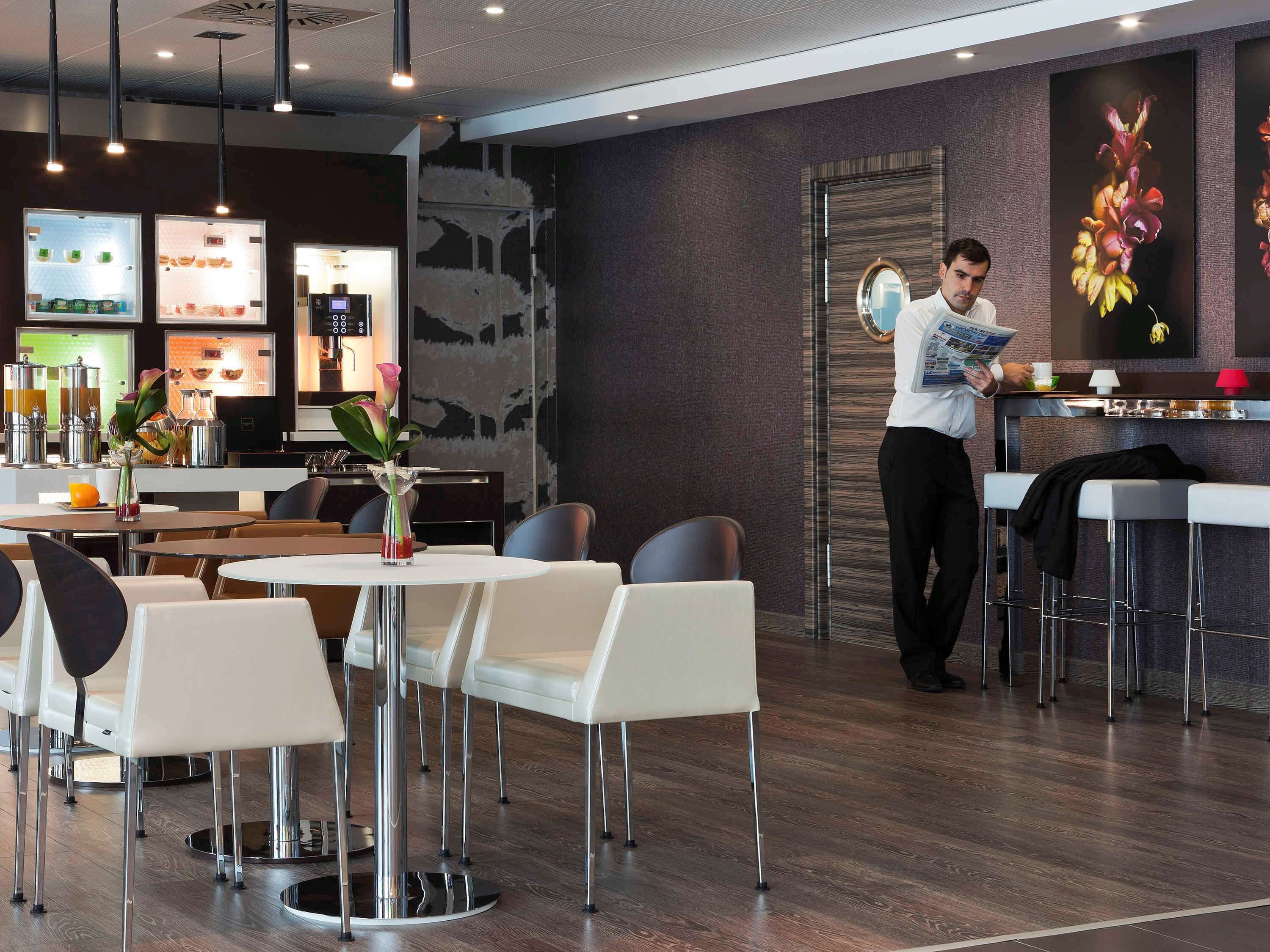 A modern hotel lobby with a reception desk, seating area, and a coffee machine.
