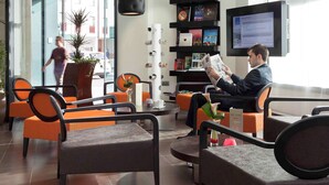 En modern hotellobby med sittgrupper, en receptionsdisk, en bokhylla med böcker och en tv-skärm.