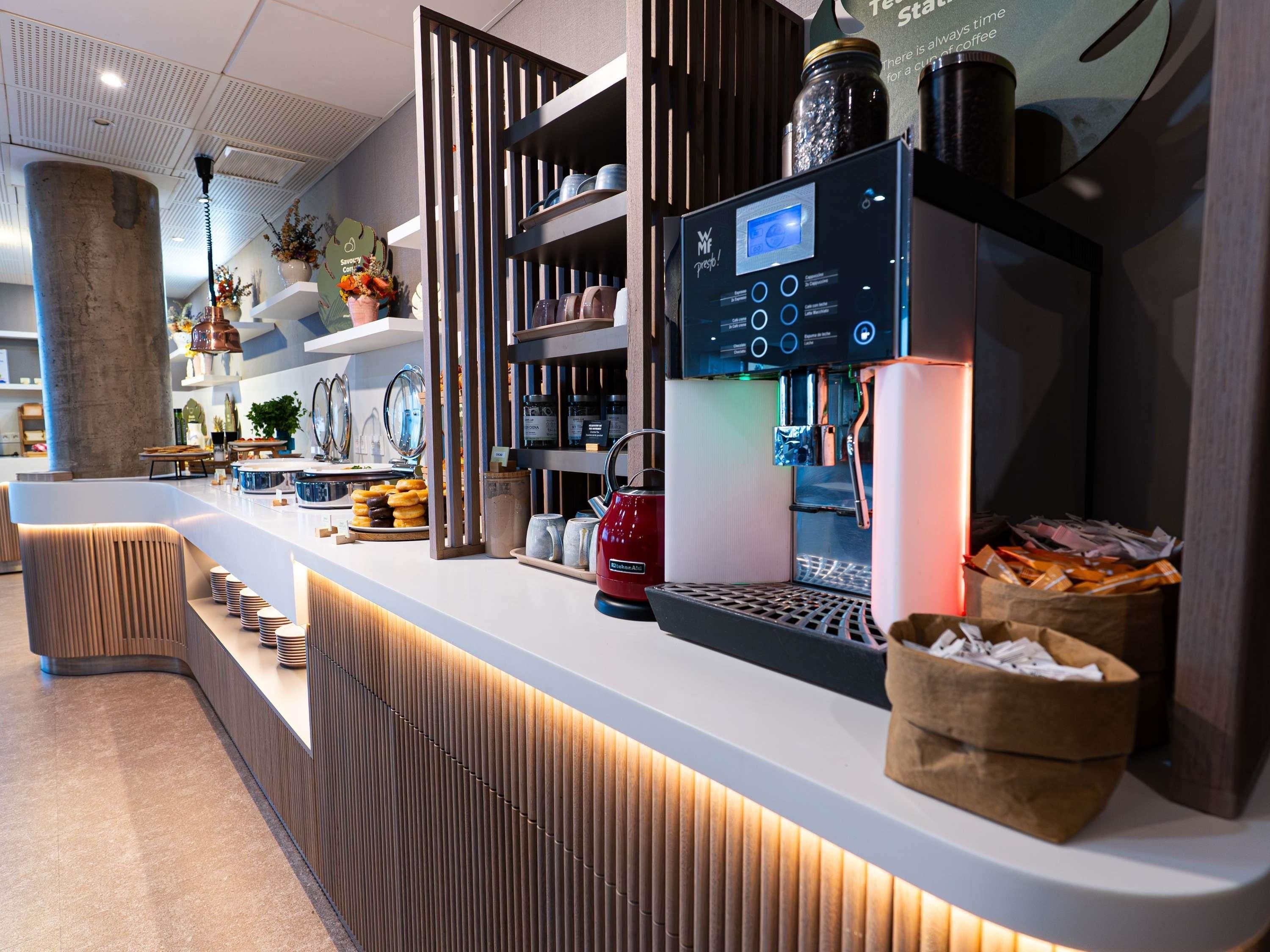 Un moderno café con una máquina de café digital, un hervidor y una bolsa de papel llena de tazas de café.