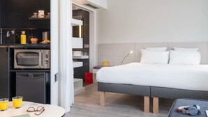 Ett modernt hotellrum med en säng, ett nattduksbord och en liten köksdel.