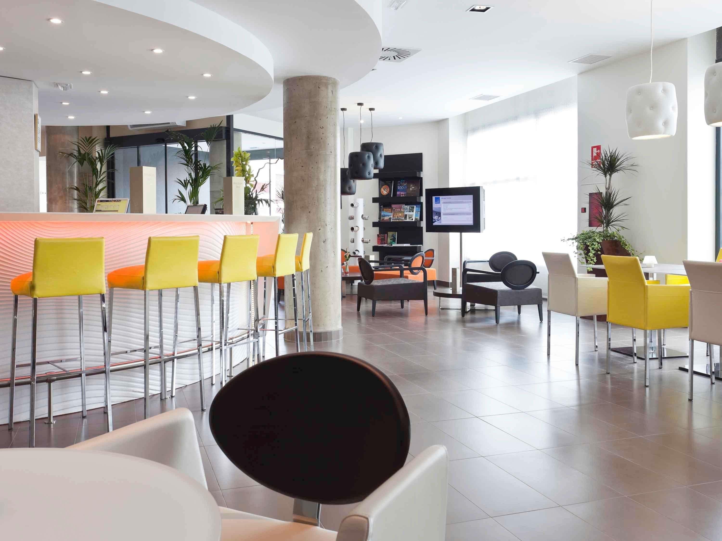 Eine moderne Hotelhalle mit einer Rezeption, gelben Barhocker und einer Sitzecke mit verschiedenen Stühlen.
