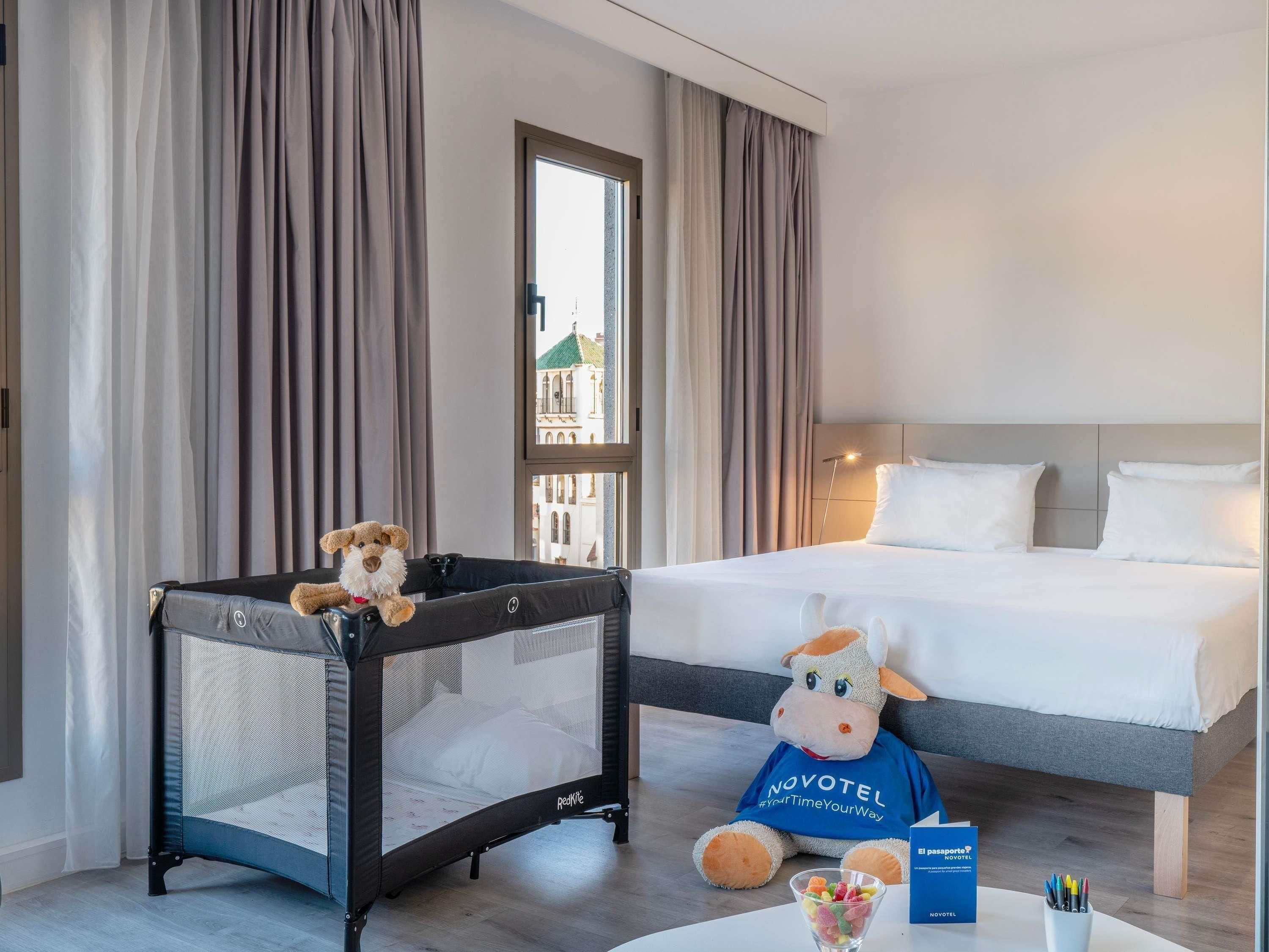 A hotel room with a bed, a crib, a stuffed toy, and a welcome booklet.