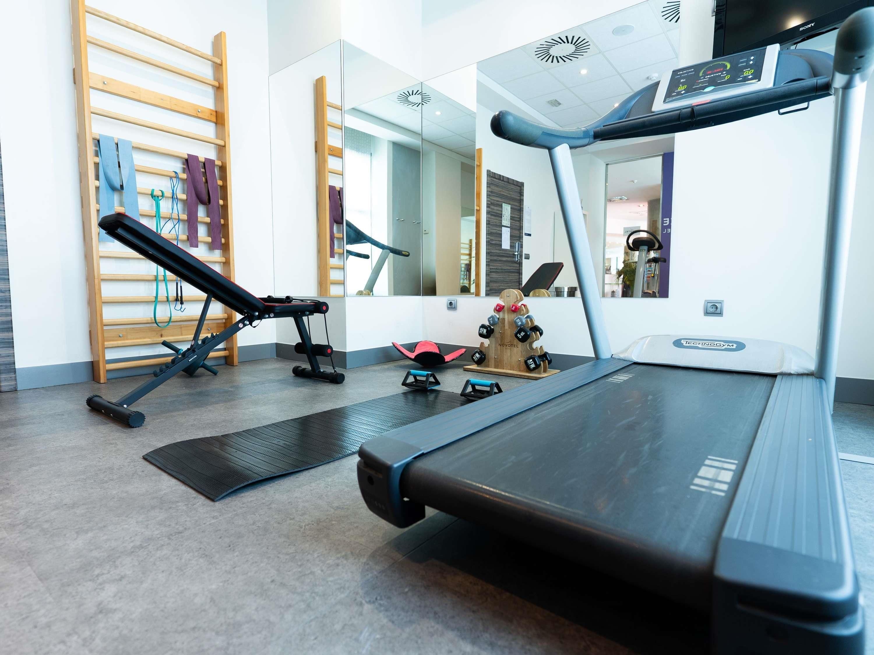 Ein Fitnessstudio mit Laufband, Trainingsgeräten und Spiegeln.