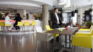 A modern hotel lobby with a reception desk, yellow and white seating, and a large table with a laptop. - Novotel Suites Malaga Centro (Málaga)